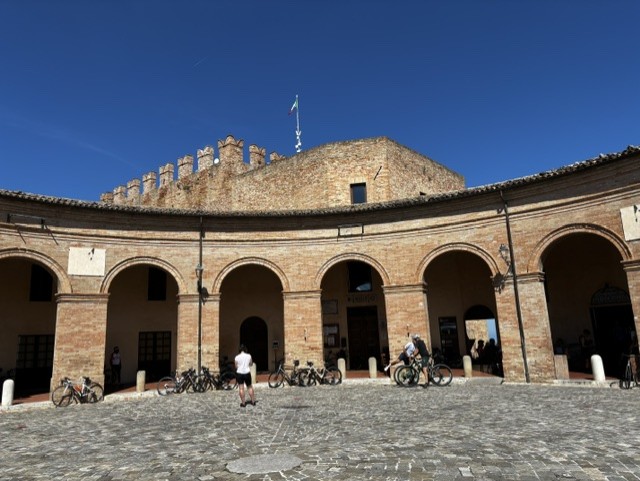 Historic courtyard with arched columns, surrounded by brick buildings, bicycles parked, under a clear blue sky.