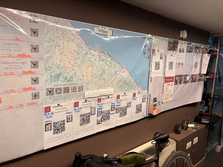 A wall display featuring a map and various printed materials related to cycling tours, including QR codes, route information, and schedule for Friday.